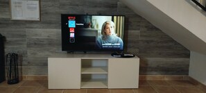 A television on a white stand in a room with a tiled floor and a wooden wall.