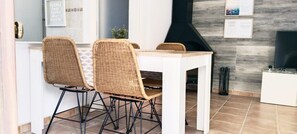 A dining area with wicker chairs, a white table, and a black grill.