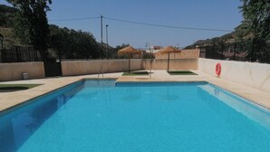 Una piscina rectangular con superficie de agua azul cristalina, rodeada por un muro bajo y una valla.