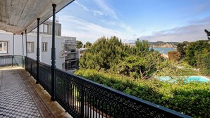 Ein Balkon mit Fliesenboden, schwarzer Brüstung und Blick auf eine Küstenlandschaft mit Bäumen und einem Schwimmbad.