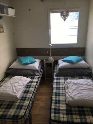A room with two beds, each with a checkered bedspread and pillows, a bedside table with a lamp, and a window with a heart-shaped decoration. - Chalet 'Strandliebe Bredene' with Private Terrace (Bredene)