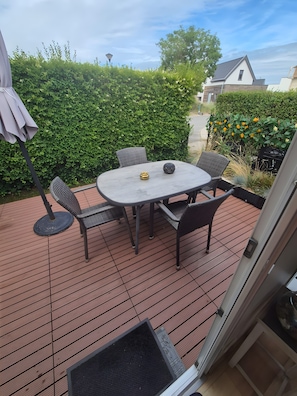 Eine Terrasse mit Tisch und Stühlen, eine Tür und ein Hecken im Hintergrund.