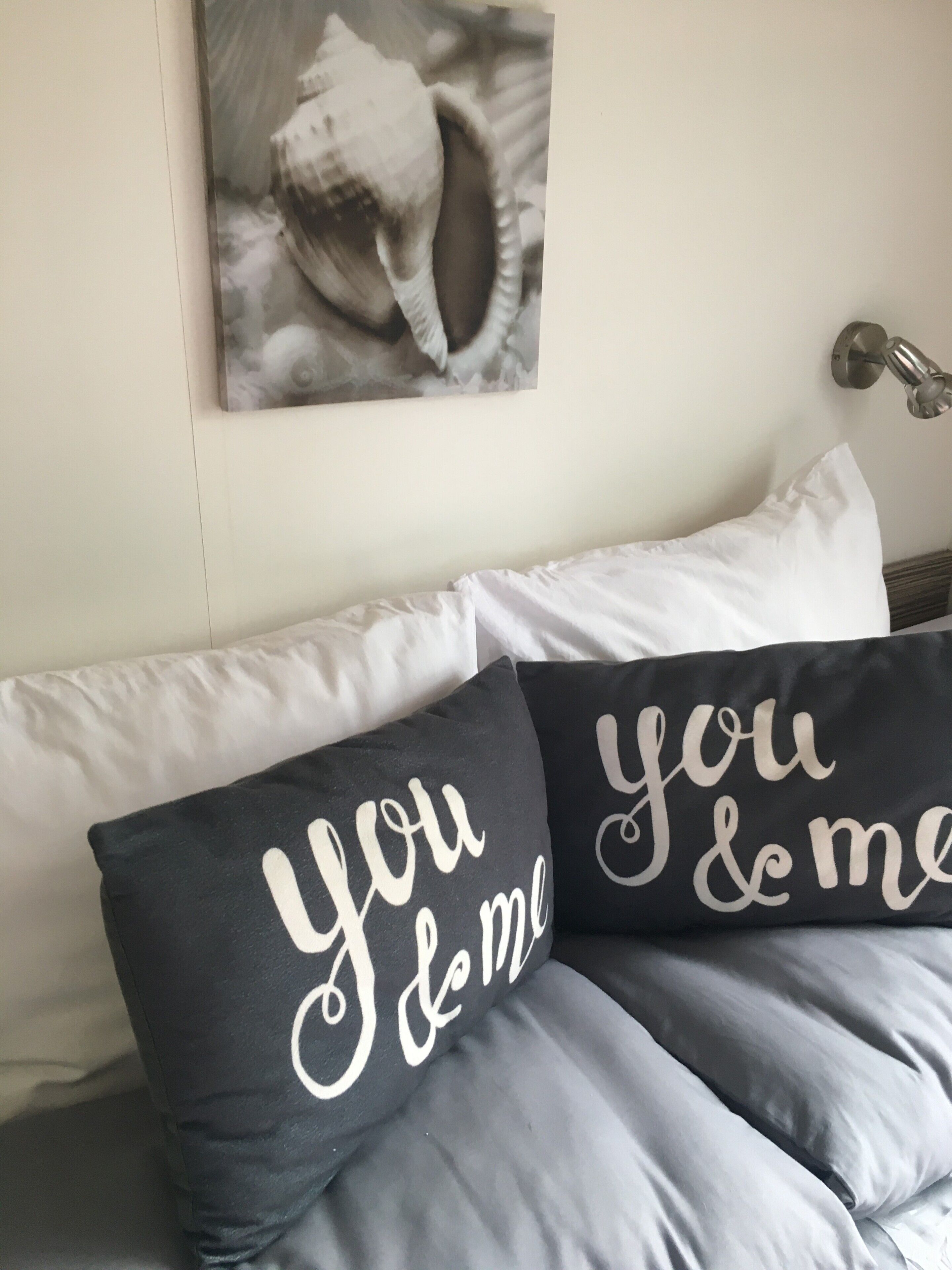 Una cama con almohadas blancas y negras, una de ellas con el texto 'you & me', y un cuadro colgado en la pared.