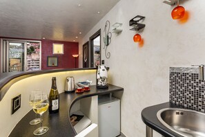A modern kitchen with a built-in coffee machine, a mini-fridge, and two wine glasses on the counter.