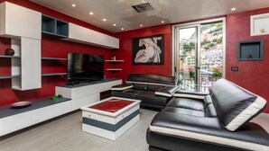 A modern living room with a flat-screen TV, black leather sofa, and a red accent wall. - Tao Rama Suite Apartment with Sea View, Wi-Fi, and Air Conditioning (Taormina)