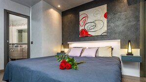 A modern bedroom with a large bed, a wall-mounted abstract painting, and a bedside table with a lamp. - Tao Rama Suite Apartment with Sea View, Wi-Fi, and Air Conditioning (Taormina)