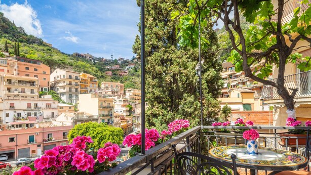 A balcony with a table and chairs, overlooking a hillside with buildings. - Tao Rama Suite Apartment with Sea View, Wi-Fi, and Air Conditioning (Taormina)
