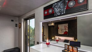 A modern hotel room with a large mirror, artwork, a bedside table with candles, and a view through the glass door. - Tao Rama Suite Apartment with Sea View, Wi-Fi, and Air Conditioning (Taormina)