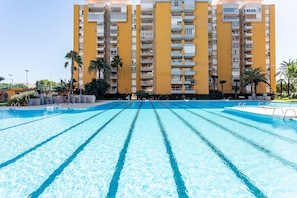 Une piscine à l’eau d’un bleu limpide, entourée d’un bâtiment jaune doté de nombreux balcons.
