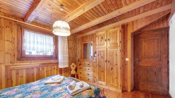 Ein Zimmer aus Holz mit einem Bett, einem Schminktisch, einer Tür und einem Fenster mit Vorhängen.