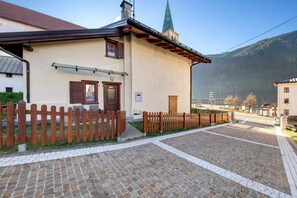 A building with a wooden fence, a paved courtyard, and a mountain in the background. - Apartment 'Villa Maria Auronzo' with Mountain View and Private Garden (Auronzo di Cadore)