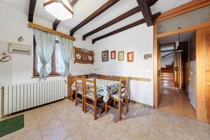 A dining area with a table, chairs, a radiator, a window with curtains, and a hallway leading to a kitchen. - Apartment 'Villa Maria Auronzo' with Mountain View and Private Garden (Auronzo di Cadore)