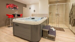 Un baño moderno con bañera de hidromasaje, zona de ducha y un área de estar con sillas rojas.