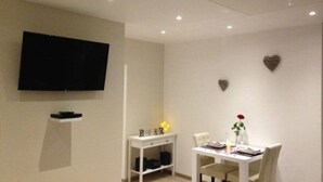 Un comedor moderno con un televisor de pantalla plana en la pared, una pequeña consola blanca y una mesa de comedor con sillas.