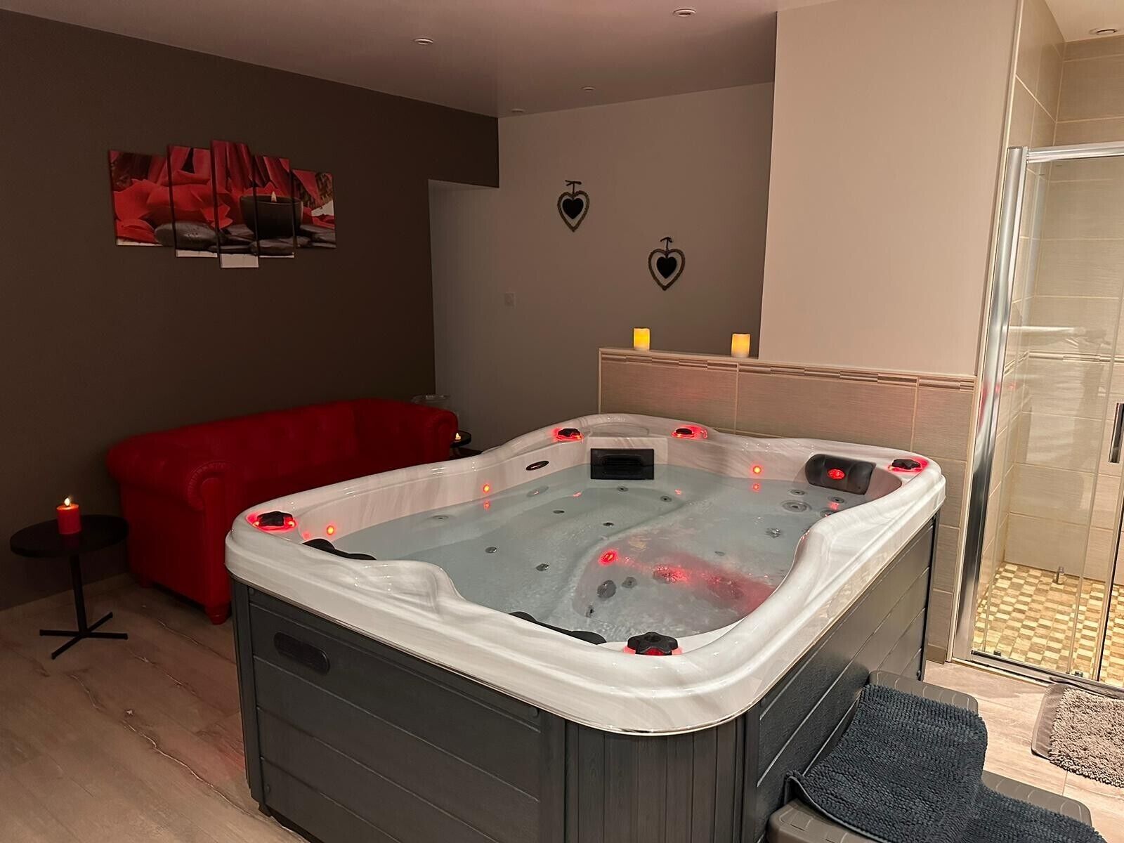 A modern bathroom with a glass shower enclosure, a red sofa, and a hot tub.