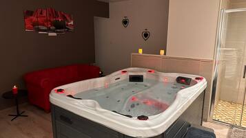 A modern bathroom with a glass shower enclosure, a red sofa, and a hot tub.