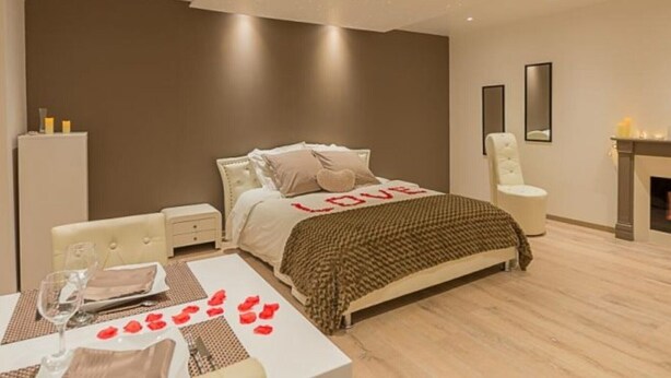 Un dormitorio moderno con cama, mesitas de noche, una silla, una pequeña mesa con un vaso y una chimenea.