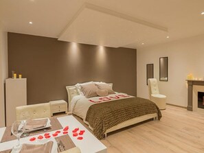 A modern bedroom with a bed, bedside tables, a chair, a small table with a glass, and a fireplace. - Love Room - Auvergne, Massif Central, at the Foot of the Volcanoes (Bort-les-Orgues)