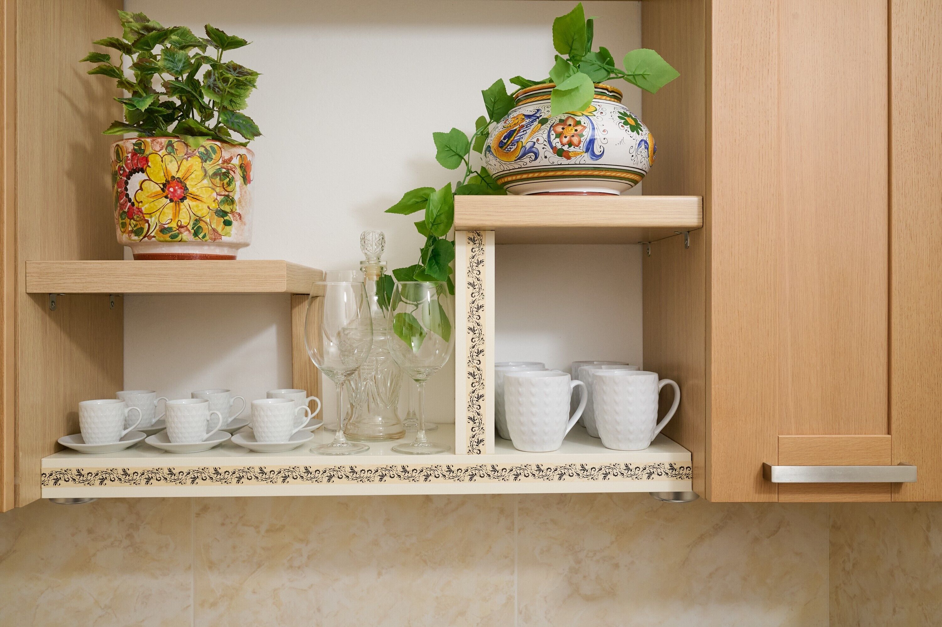 Een keukenkastje met een bloempot, een decoratieve vaas en witte keramische bekers en glazen.