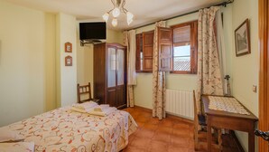 Un dormitorio con cama, escritorio, silla, armario, televisor y ventana con cortinas.