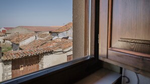 Vista por la ventana de un edificio con techo de tejas, una puerta de madera y una pequeña señal en la pared.