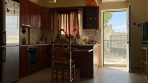 A kitchen with wooden cabinets, a refrigerator, an oven, a sink, and a dining area with a chair. - Apartment 'Spitiko  1' with Sea View, Shared Terrace and Wi-Fi (????????)