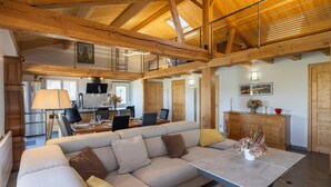A spacious living area with a high ceiling, wooden beams, a sofa, a dining table, and a kitchen in the background. - Holiday Home 'Maison Chalet' with Mountain View, Private Terrace and Wi-Fi (Le Nayrac)