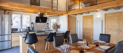 Una cocina moderna con comedor, vigas de techo de madera y vistas al exterior.