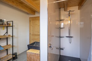 A bathroom with a shower, wooden shelves, and a black countertop.