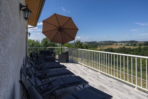 Ein Balkon mit Liegestühlen und Sonnenschirm, mit Blick auf eine reizvolle Landschaft.