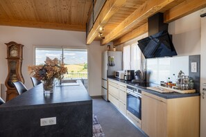 Eine moderne Küche mit Kochinsel, Holzschränken, integriertem Backofen und großem Fenster mit Blick ins Freie.