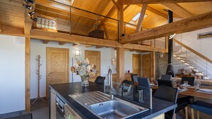 A modern kitchen with a large island, wooden beams, and a dining area with a staircase. - Holiday Home 'Maison Chalet' with Mountain View, Private Terrace and Wi-Fi (Le Nayrac)