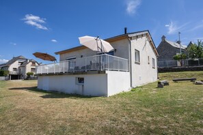 Ein eingeschossiges Haus mit einem Balkon, einem weißen Sonnenschirm und einem Steinhaus im Hintergrund.