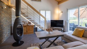 A modern living room with a fireplace, a sofa, a TV, and a staircase. - Holiday Home 'Maison Chalet' with Mountain View, Private Terrace and Wi-Fi (Le Nayrac)