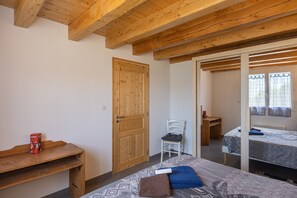 Ein Zimmer mit Holzbalken, einem Bett, einem Sessel, einem Schreibtisch und einem Kleiderschrank.