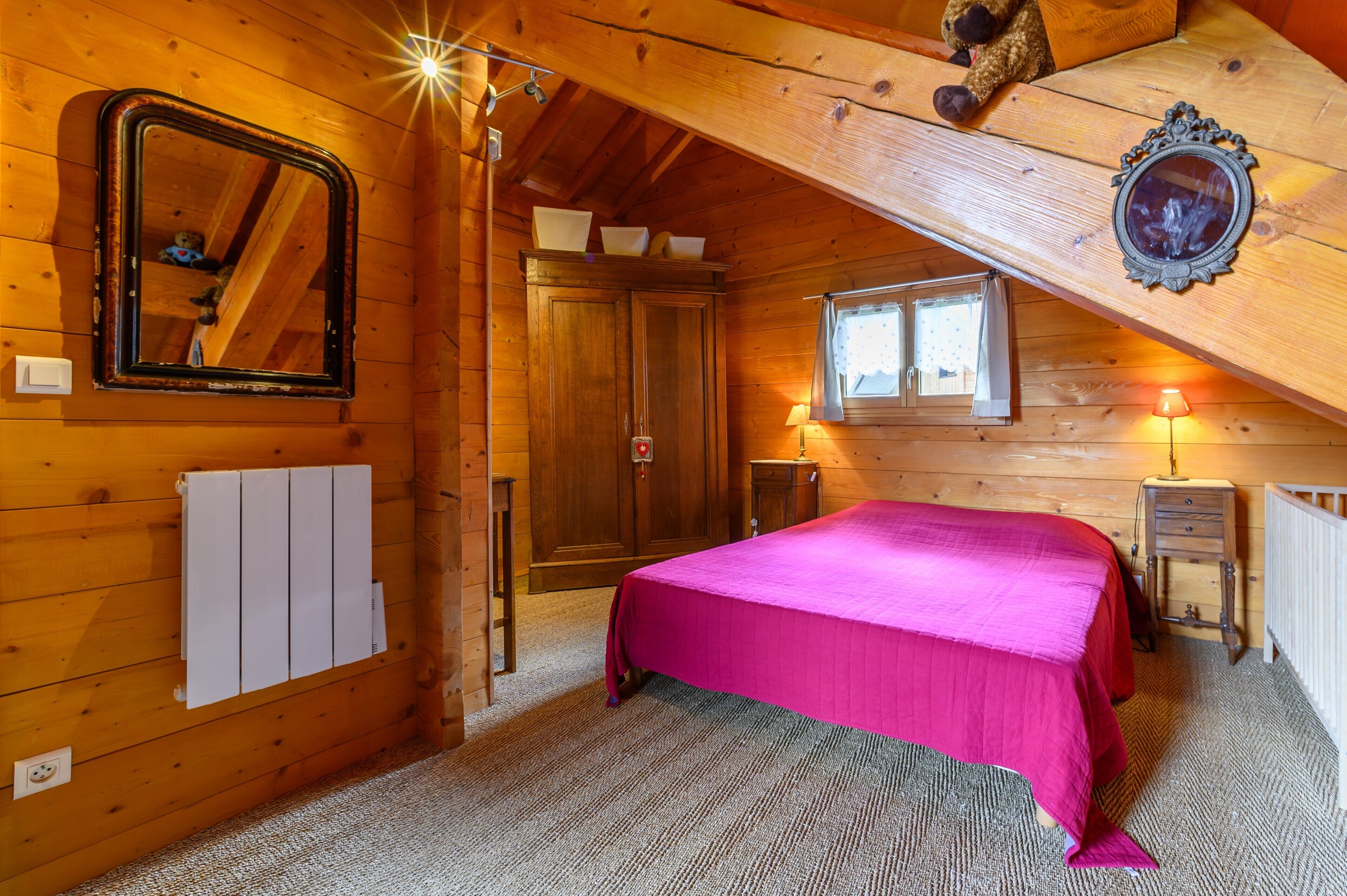 Ein Zimmer mit Holzboden, einem Bett, einem Spiegel, einem Fenster und einer Heizung.