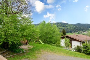 Un paysage rural avec une maison en bois, une balançoire et une vue sur une colline boisée.