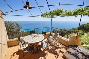 A terrace with a table and chairs, a hanging light fixture, and a view of the sea. - Apartment 'Mandarino' with Sea View, Wi-Fi and Air Conditioning (Finale Ligure)