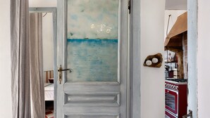A room with a view through a door, a bed, a red stove, and a wall-mounted shelf with items. - Apartment 'Nespolo' with Sea View, Wi-Fi and Air Conditioning (Finale Ligure)