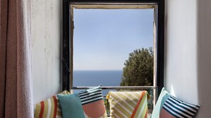 A window with a view of the sea, a sofa with striped cushions, and a curtain. - Apartment 'Nespolo' with Sea View, Wi-Fi and Air Conditioning (Finale Ligure)