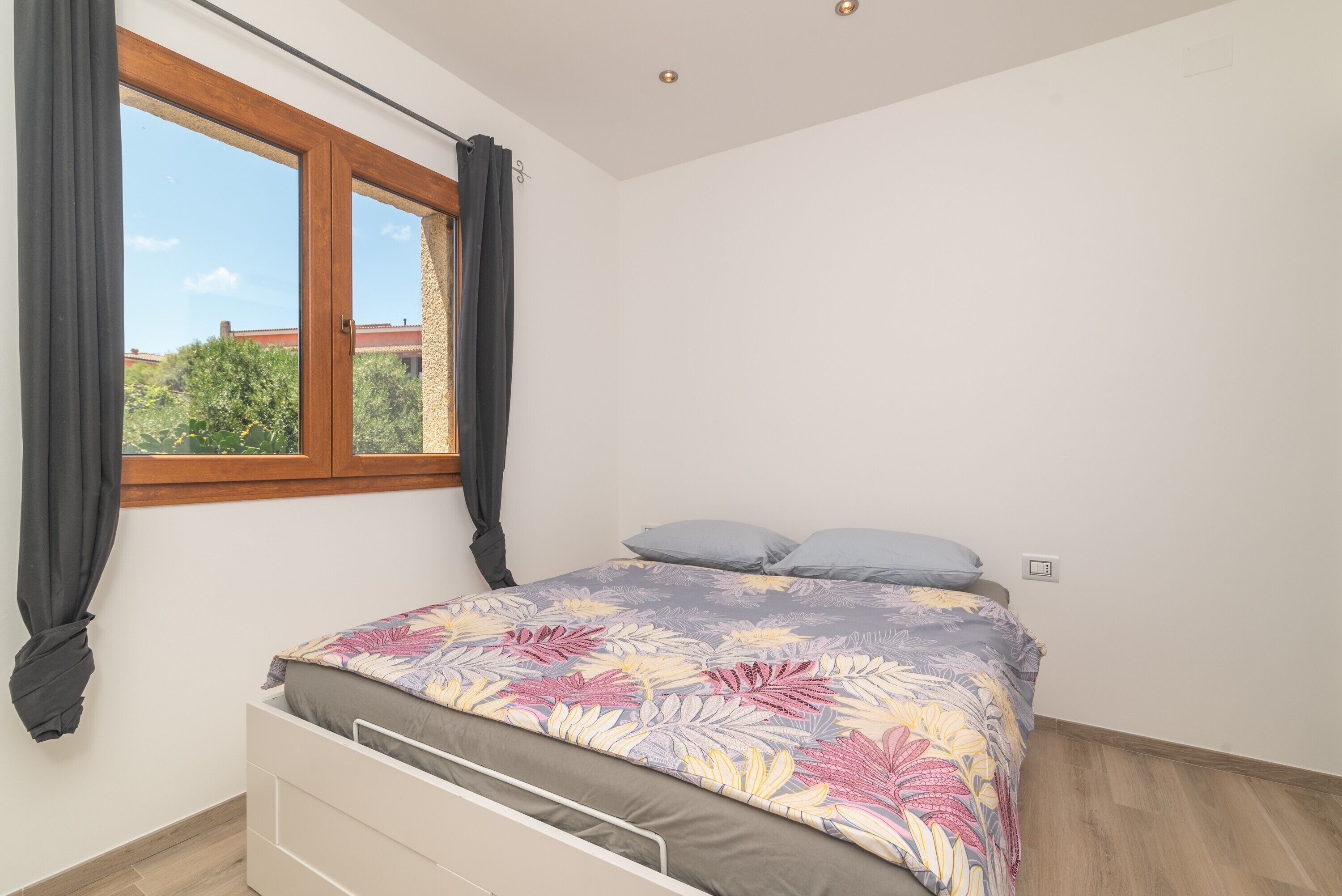 Une chambre à coucher avec un lit, une fenêtre avec des rideaux et une vue sur la verdure.