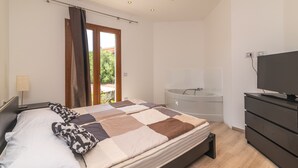 Un dormitorio con cama, televisión, bañera y ventana con cortinas.