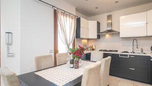 Una cocina moderna con comedor, que incluye una mesa con posavasos, sillas, un jarrón con flores y una encimera con electrodomésticos.