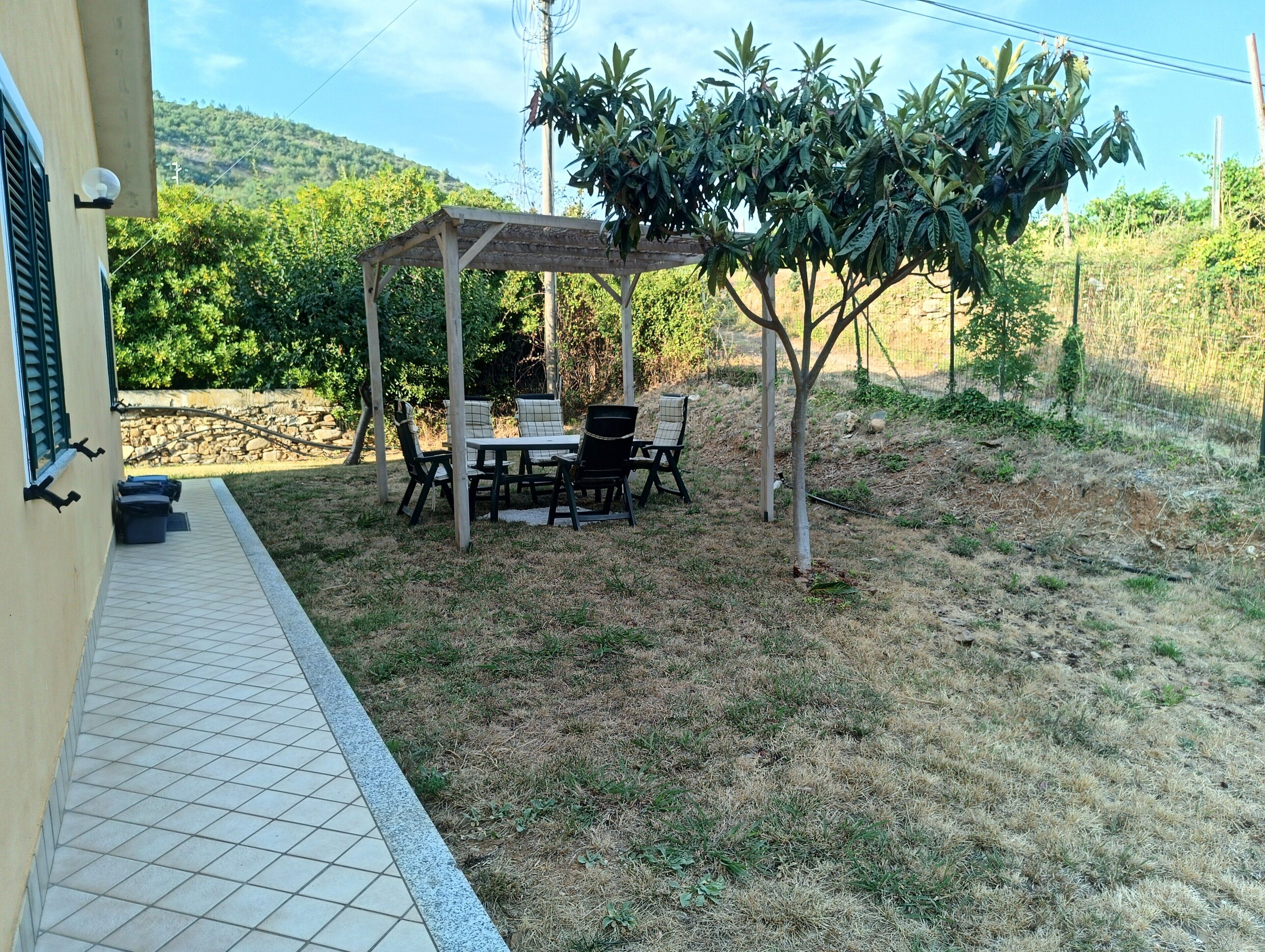 Eine Terrasse mit Tisch, Stühlen, einer Pergola und einem kleinen Baum.
