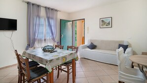 A dining area with a table and chairs, a sofa, and a television mounted on the wall. - Villa 'Il Frutteto 50' with Private Terrace and Wi-Fi (Ortovero)