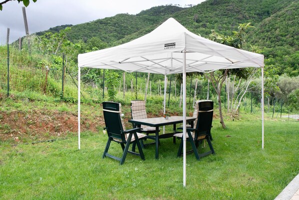 Ein Zelt mit Tisch und Stühlen im Freien, umgeben von Grün und Hügeln.