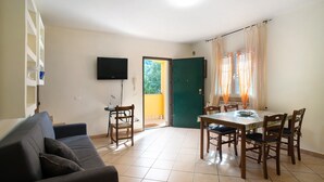 Un salon comprenant un canapé, une table à manger avec des chaises, un téléviseur fixé au mur et une porte donnant sur l’extérieur.