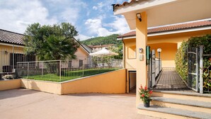 Une cour avec un bâtiment jaune, une clôture en métal et un escalier menant à une entrée fermée par un portail.