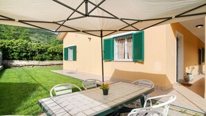 Une terrasse avec une table et des chaises, un pot de fleurs et une vue sur une pelouse verdoyante et une colline.