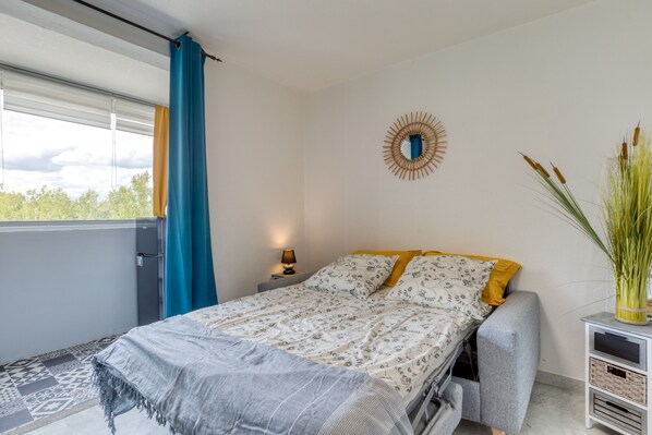 Une chambre à coucher comprenant un lit, une table de chevet, une lampe, un miroir décoratif et une vue sur l’extérieur.